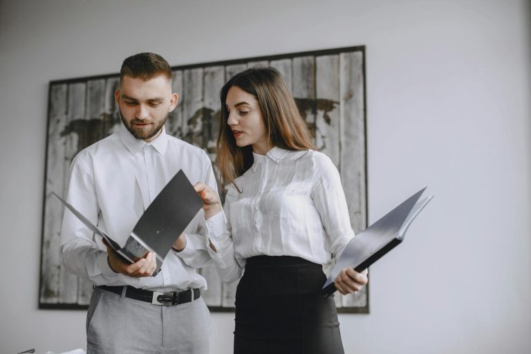 Two colleagues in a modern office reviewing documents together.